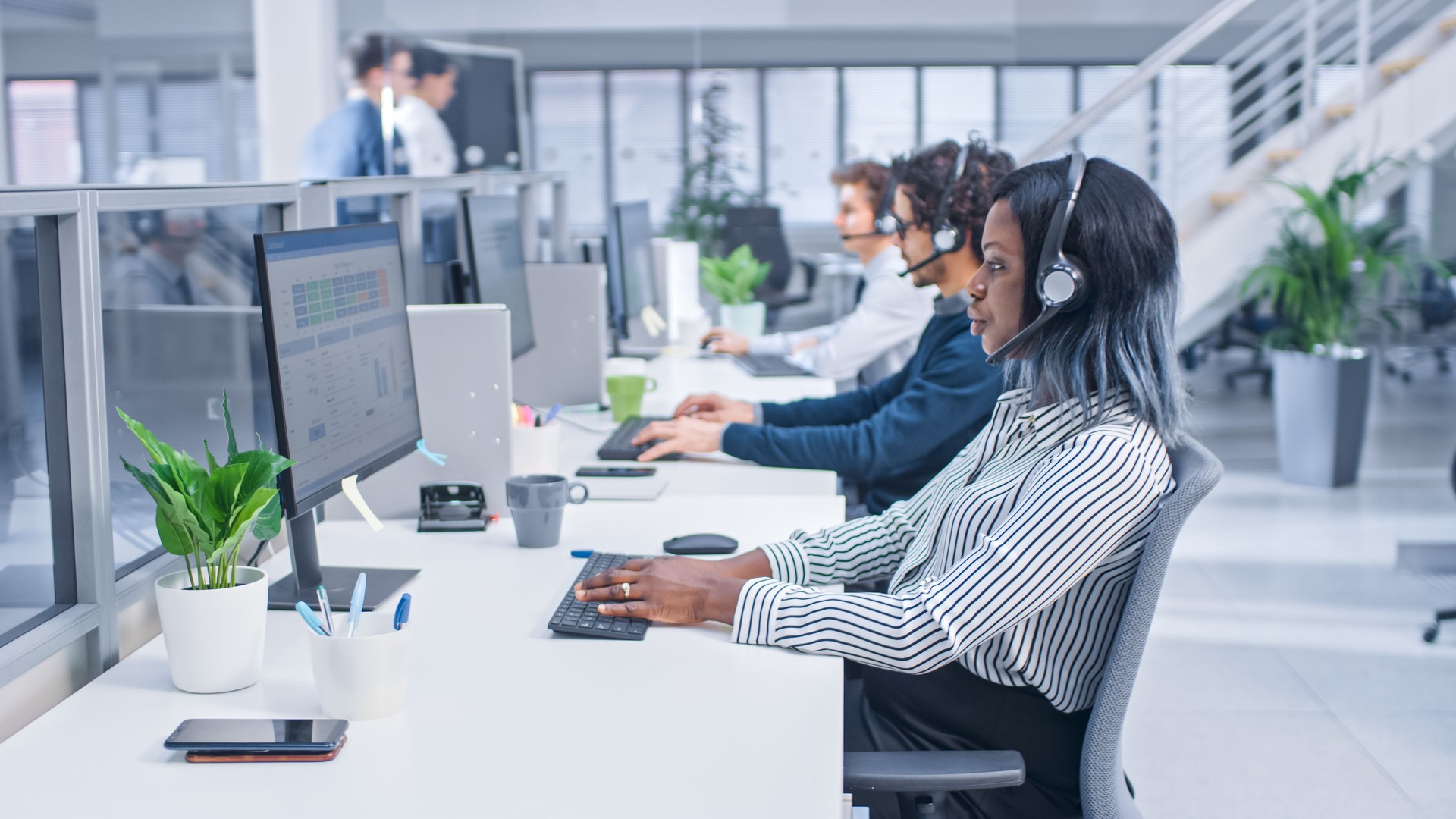 Team of Handsome and Beautiful Diverse Multicultural Customer Service Operators Working at a Busy Modern Call Center with Specialists Wearing Headsets and Actively Taking Calls.